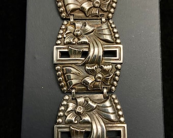 Könnte beinhalten: Ein silbernes Armband mit floralem Design. Das Armband besteht aus mehreren Gliedern, jedes mit einem geprägten Blumenmuster.