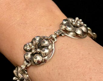 Könnte beinhalten: Ein silbernes Armband mit floralem Design. Das Armband besteht aus mehreren miteinander verbundenen, blütenförmigen Gliedern.