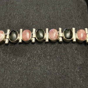 May include: A silver bracelet with alternating black and pink oval stones. The bracelet has a link style design.