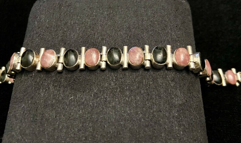 May include: A silver bracelet with alternating black and pink oval stones. The bracelet has a link style design.
