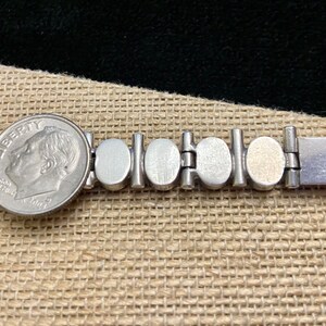 May include: A silver bracelet with a series of round, silver-toned links. The bracelet has a clasp with the inscription "950" on the back.