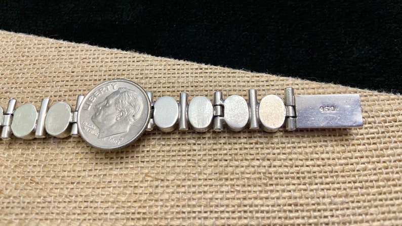 May include: A silver bracelet with a series of round, silver-toned links. The bracelet has a clasp with the inscription "950" on the back.