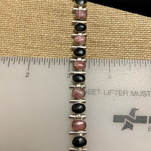 May include: A silver bracelet with alternating black and pink oval stones. The bracelet is about 6 inches long.