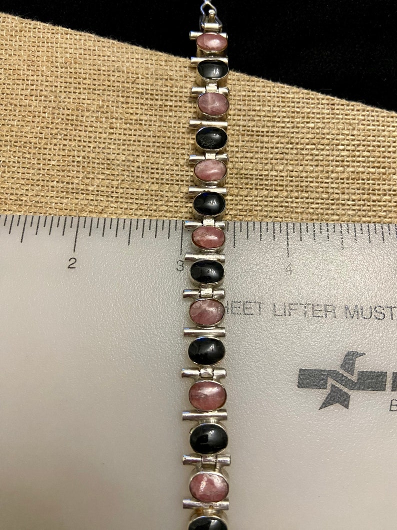 May include: A silver bracelet with alternating black and pink oval stones. The bracelet is about 6 inches long.