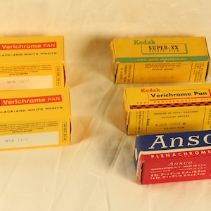 May include: Four boxes of Kodak Verichrome Pan film for black and white prints, one box of Kodak Super-XX high speed panchromatic film, and one box of Ansco Plenachrome film. The boxes are yellow, red, and blue with black and white text.