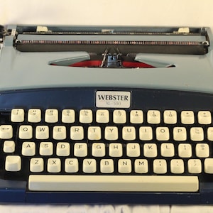 May include: A blue and black vintage Webster XL-500 typewriter with a white keyboard and a red tab key.