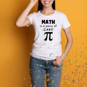 May include: A white t-shirt with the text "MATH is a piece of CAKE - PI" printed on it. The person wearing the shirt is smiling and standing in front of a yellow background.