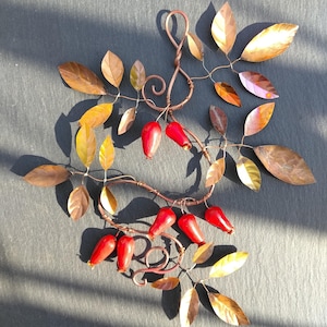 May include: A decorative wall hanging featuring a copper wire branch structure with twisted stems and curls. The piece is adorned with numerous metallic copper-coloured leaves and several smooth, bright red, teardrop-shaped berry ornaments.