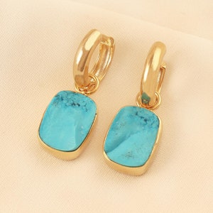 May include: A pair of gold hoop earrings with turquoise stone drop pendants. The stones are a light blue color and have a slightly textured surface.