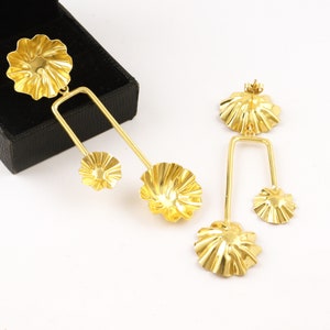 May include: A pair of gold-tone earrings with a geometric design. Each earring features three flower-shaped charms, two smaller charms and one larger charm.