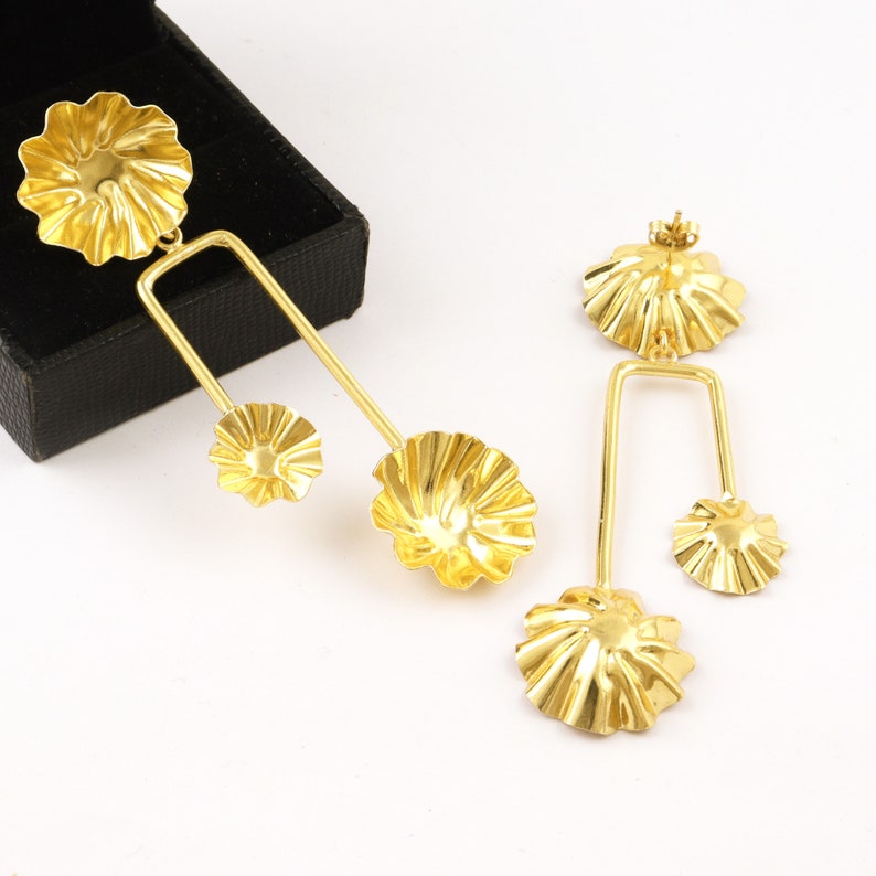 May include: A pair of gold-tone earrings with a geometric design. Each earring features three flower-shaped charms, two smaller charms and one larger charm.