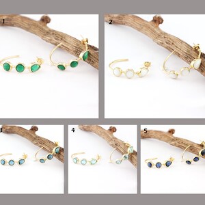 Op de afbeelding: Vijf paar gouden creolen met verschillende gekleurde edelstenen. Elk paar heeft vier edelstenen in een rij. De edelstenen zijn groen, wit, blauw, lichtblauw en donkerblauw.