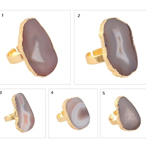 May include: Five adjustable rings featuring large, irregular, polished agate slices in shades of gray, brown, and white. Each stone is encased in a gold-toned metal rim with a matching gold-toned band. The rings are numbered one through five.