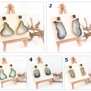 May include: Five pairs of agate earrings with gold accents. Each pair is displayed on a small wooden easel. The earrings are all different colors and patterns.