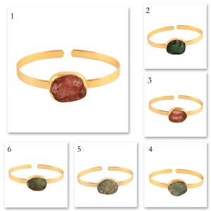 Könnte beinhalten: Sechs goldene Armbänder mit verschiedenen farbigen Edelsteinen. Die Armbänder sind alle im gleichen Stil gehalten, mit einem dünnen goldenen Band und einem großen, ovalen Edelstein in der Mitte. Die Edelsteine sind rosa, grün und hellgrün.