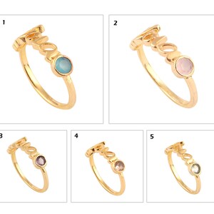 May include: Five gold rings with the word "Mama" spelled out on the band. Each ring has a different colored gemstone: turquoise, pink, purple, light pink, and green.