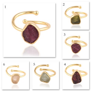 Peut inclure: Une collection de six bagues réglables dorées, chacune ornée d'une pierre précieuse brute et irrégulière de différentes couleurs, notamment rouge foncé, vert olive, bordeaux, vert pâle et rose clair translucide, sertie dans un chaton.