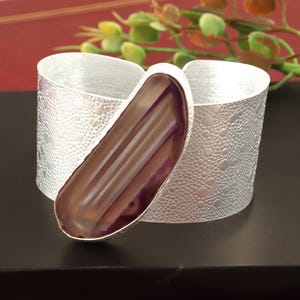 May include: A silver cuff bracelet with a large, purple agate stone set into the metal. The stone has a striated pattern and a smooth, polished finish.