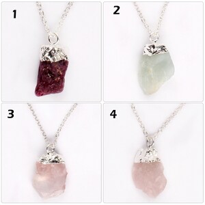 May include: Four necklaces with raw gemstone pendants. Each pendant is a different color: a deep red, a pale green, and two shades of pink. The gemstones are attached to silver-colored chains with silver-colored metal caps.