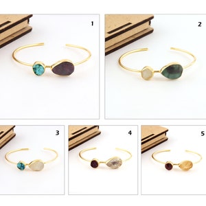 May include: Five gold-toned open cuff bracelets, each featuring two distinct raw-cut stones in various colors including turquoise, deep red, green, and translucent white. The bracelets are numbered one through five, showcasing different gemstone pairings.