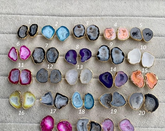 May include: A selection of 23 pairs of gemstone stud earrings. Each earring has a unique, irregularly shaped stone with a gold-coloured metal border. The stones vary in colour, including grey, blue, pink, purple, and orange.