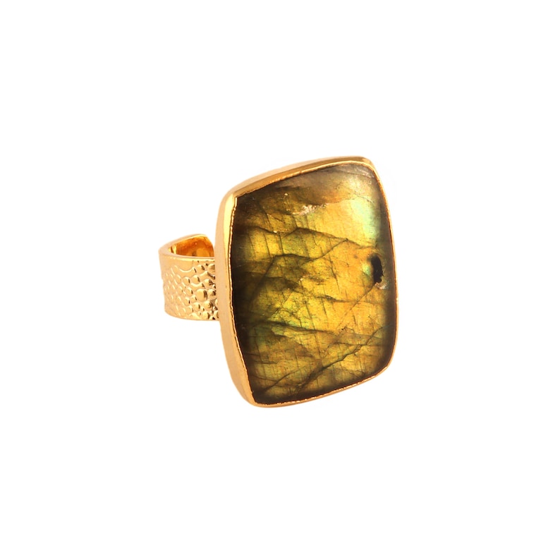 Puede incluir: Un anillo de oro con una gran piedra preciosa de labradorita de forma cuadrada. La piedra preciosa es una mezcla de colores verdes y dorados con un acabado brillante e iridiscente.
