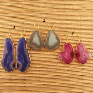 May include: Four pairs of agate earrings with gold-tone hooks. The earrings are in the shapes of teardrops and hearts. The agate is in shades of blue, pink, and green.