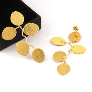 May include: A pair of gold earrings with a branch-like design and multiple round discs. The earrings are made of a textured metal.