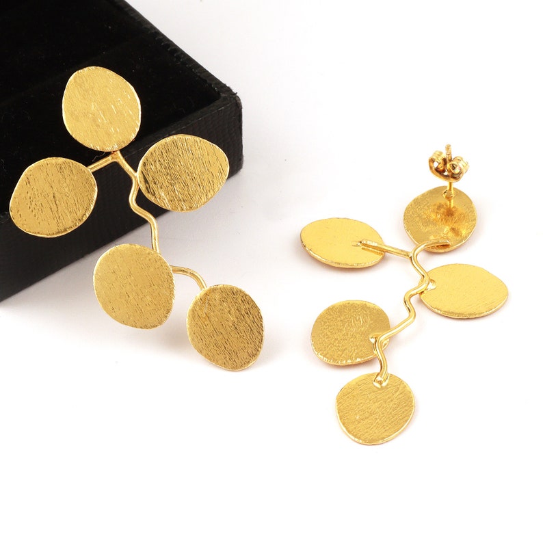 May include: A pair of gold earrings with a branch-like design and multiple round discs. The earrings are made of a textured metal.