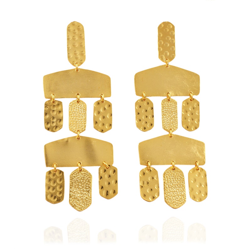 May include: A pair of gold-toned dangle earrings with a geometric design. The earrings feature multiple tiers of rectangular and teardrop-shaped pieces, each with a textured surface.