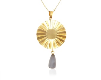 May include: Gold necklace with a large, round pendant featuring a sunburst design and a small, teardrop-shaped gray stone hanging from the bottom.