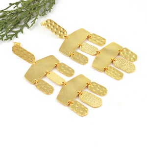 May include: A pair of gold-tone geometric dangle earrings with a hammered texture. The earrings are made of multiple rectangular and oval shapes.