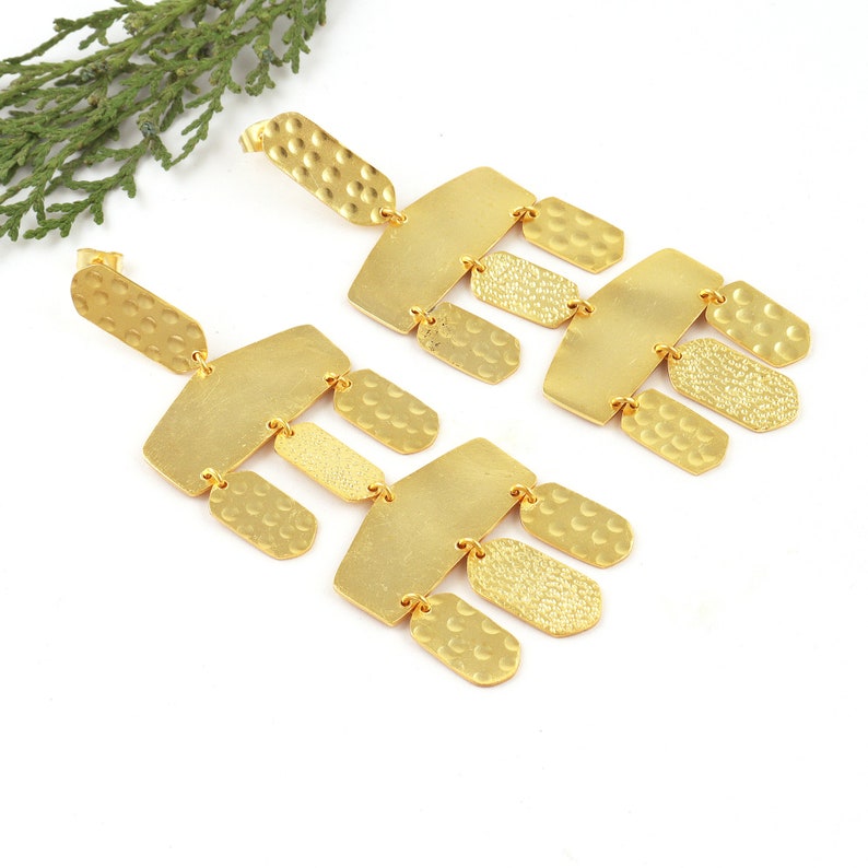 May include: A pair of gold-tone geometric dangle earrings with a hammered texture. The earrings are made of multiple rectangular and oval shapes.