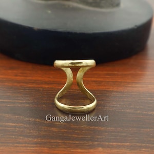 May include: A gold-colored ring with a unique design. The ring features a flat, horizontal band connected to a curved base, creating an open, geometric shape. The ring is likely made of metal and has a polished finish. The text "GangaJewellerArt" is visible.