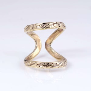 May include: A gold-toned ring with a floral design. The ring is open and has a unique, curved shape.
