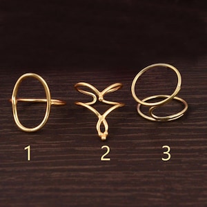 May include: Three gold rings with different designs. The first ring is a simple oval shape. The second ring has a more intricate design with two curved lines that meet in the middle. The third ring is a double ring with one ring wrapped around the other.