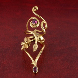May include: A gold ring with a vine design and three purple gemstones. The ring is open and adjustable.