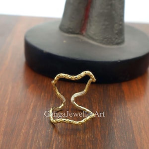 May include: Gold-toned ring with a wavy, textured design. The ring is open and adjustable.