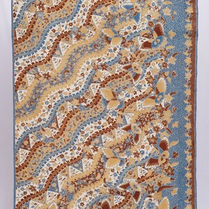 Puede incluir: Textil rectangular con un detallado estampado floral en tonos beige, marrón y azul. El diseño presenta flores estilizadas y líneas onduladas sobre un fondo blanco, con un borde azul. La tela es probablemente de algodón o similar.