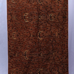 Puede incluir: Un textil marrón con un intrincado patrón de motivos florales y de hojas. El diseño presenta acentos crema y negros, creando una superficie detallada y visualmente rica. La tela se muestra verticalmente.