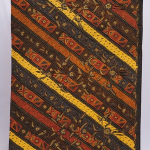 以下が含まれることがあります： 斜めストライプ模様の長方形の織物。ストライプは、濃い茶色、黄色、オレンジ色、濃い青色を交互に繰り返します。デザイン全体に花柄と幾何学模様が散りばめられています。端は赤い縁取りで仕上げられています。