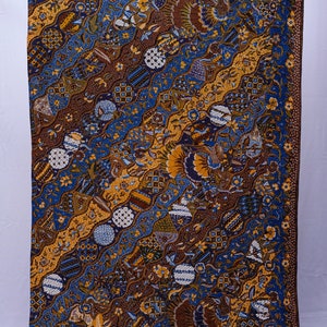 May include: A rectangular textile with a vibrant, intricate pattern. The design features diagonal bands of blue, brown, and gold, adorned with floral and geometric motifs. The fabric appears to be a batik, showcasing detailed artistry and a rich colour palette.