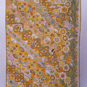 May include: A vibrant textile featuring a repeating pattern of flowers, birds, and geometric shapes in yellow, orange, pink, and blue. The fabric has a detailed design, with a dark border along one edge.