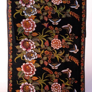 Könnte beinhalten: Schwarzer Stoff mit einem Blumen- und Schmetterlingsmuster. Das Design zeigt große, mehrfarbige Blumen in Rot-, Weiß- und Blautönen sowie Schmetterlinge und grünes Laub. Ein dekorativer Rand umrahmt die Kanten.