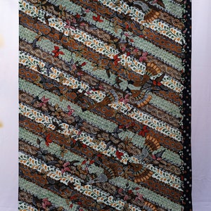 Puede incluir: Una tela estampada con un diseño diagonal. La tela presenta rayas alternas en marrón, verde y blanco, adornadas con motivos florales y de aves. Los bordes son negros con lunares blancos. El diseño general es intrincado y colorido.