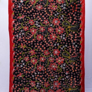 Może przedstawiać: Czarny materiał z żywym wzorem kwiatowym. Czerwone kwiaty i zielone liście są rozrzucone po tkaninie, z czerwonym obramowaniem. Wzór zawiera małe białe kwiaty i skomplikowane detale.