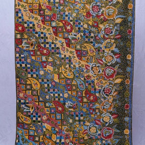 Könnte beinhalten: Ein farbenfrohes Textil mit einem detaillierten Muster. Das Design zeigt Paisley-Formen, florale Motive und geometrische Quadrate in Gelb-, Rot-, Blau- und Grüntönen. Der Stoff hat einen dunkelgrünen Rand.