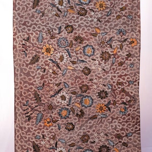 Puede incluir: Textil rectangular con un patrón floral repetido en marrón, naranja y azul sobre un fondo marrón rojizo. El fondo tiene un patrón de puntos. El textil se muestra verticalmente.