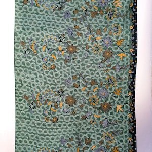 May include: Green fabric featuring a repeating pattern of interlocking circles. The fabric is adorned with floral designs in brown, yellow, and purple. A dark border with small white dots runs along one edge.