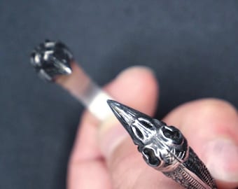 May include: A silver bracelet with two skull-shaped ends. The bracelet is open and the ends are facing each other.